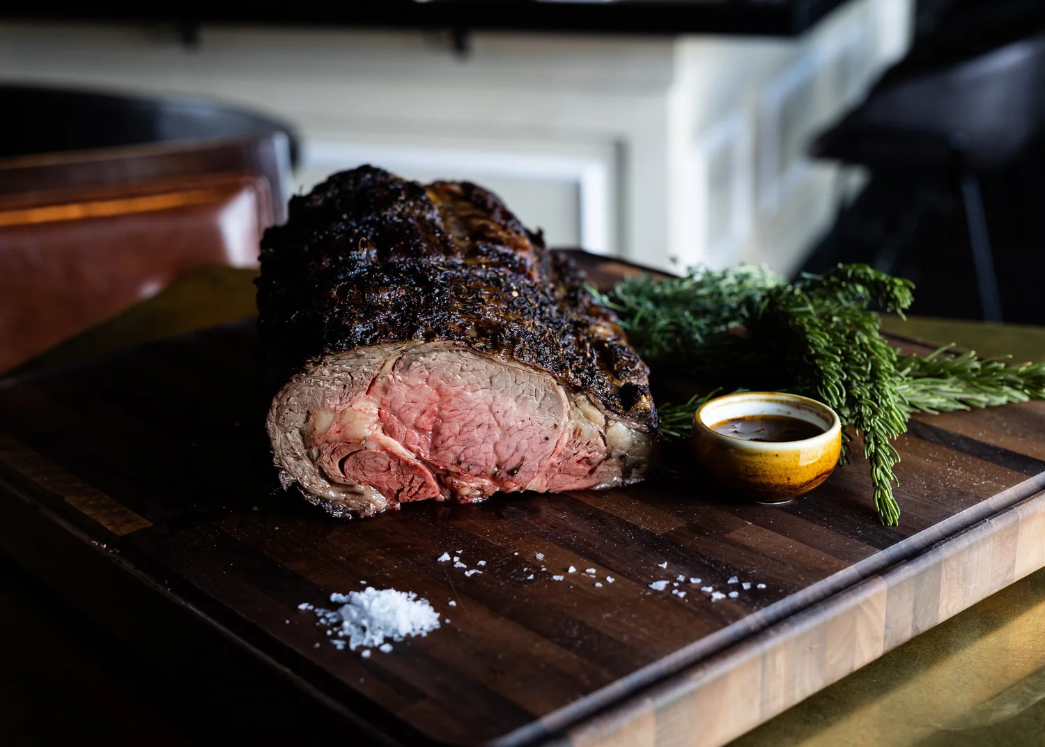 Wood-fire-roasted prime rib on a carving board with jus and flaky salt at notable - The Steakhouse