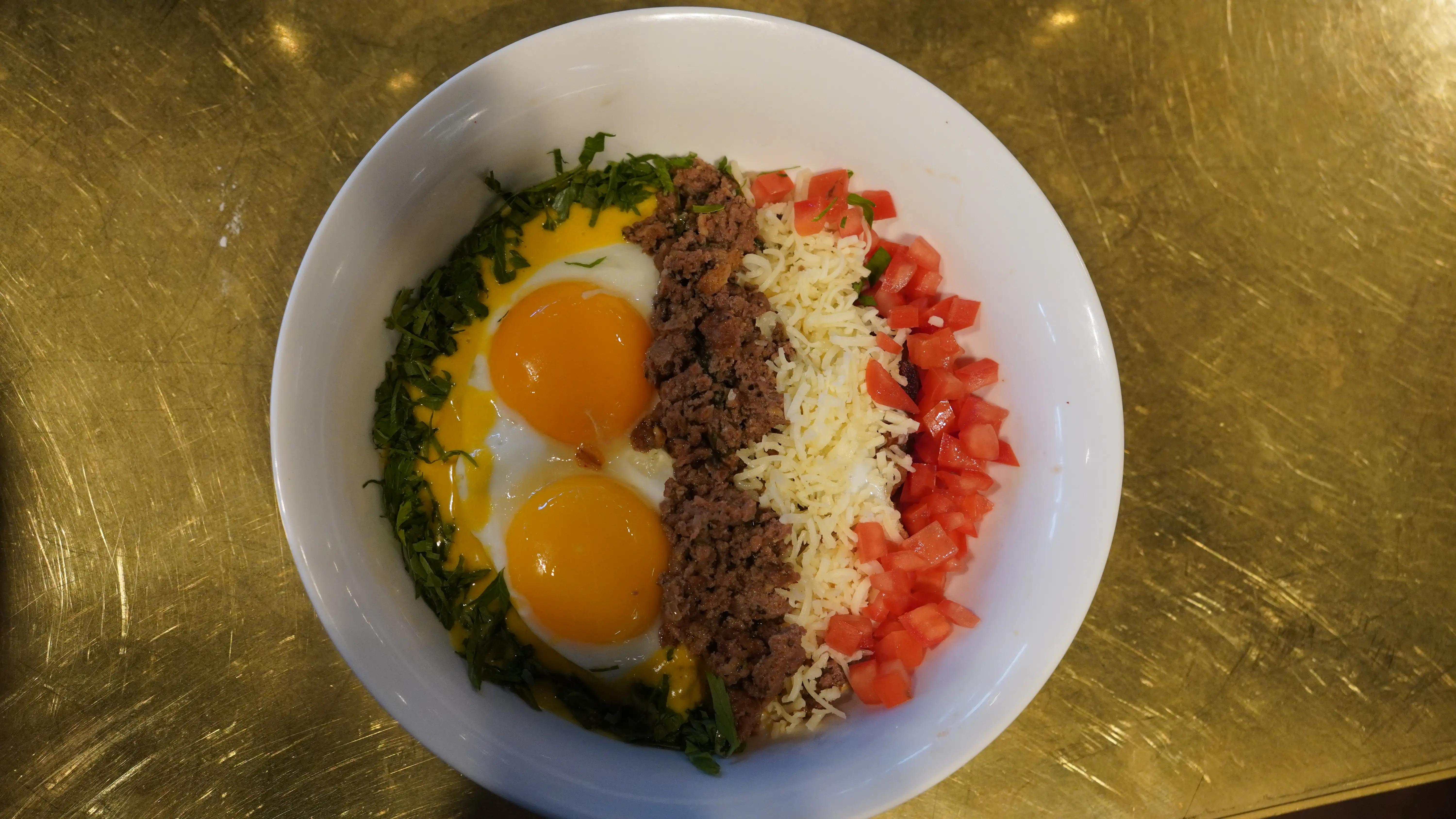 A composed bowl of eggs, seasoned Alberta beef, grated cheese, tomato and greens at notable - The Steakhouse in Montgomery, Calgary
